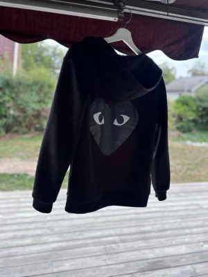Comme des Garçons - Säljer en Comme des Garçons. På ryggen finns ett stort hjärta med ögon, vilket ger en cool och unik look. Hoodien har ribbade muddar vid ärmslut och nederkant. Perfekt för dig som vill sticka ut lite extra. Priset är inte fast.