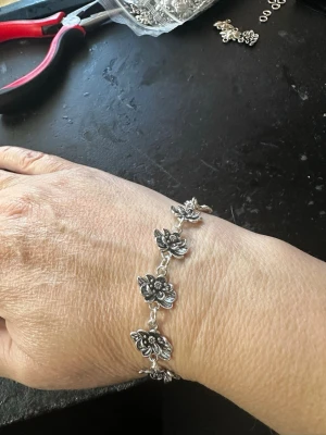 Silverfärgat armband med blommor - Snyggt armband i silverfärg med flera detaljerade blomformade länkar. Blommorna har en cool, antik finish och sitter ihop med små ringar. Perfekt för dig som gillar unika accessoarer med lite boho-vibe.