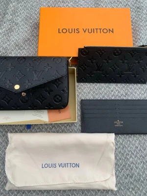Svart Louis Vuitton handväska i läder - Snygg svart handväska från Louis Vuitton i präglat läder med klassiskt monogrammönster. Väskan har guldfärgad kedja och tryckknapp. Medföljer matchande plånbok och kortfodral samt originalförpackning och dustbag.