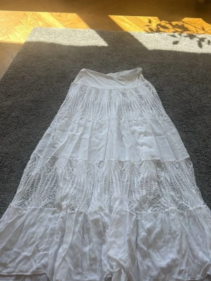 Vit långkjol med spetsdetaljer på framsida  - Vit lång kjol köpt i Spanien, one size. Jag har storlek M och passar bra. Aldrig använda då det inte är min stil 