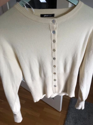 Gul kofta från Gina Tricot - Snygg gul kofta från Gina Tricot med rund halsringning och pärlemorknappar framtill. Koftan har långa ärmar och bred ribbstickad mudd vid midjan och ärmsluten. Perfekt att styla till jeans eller kjol för en clean look.