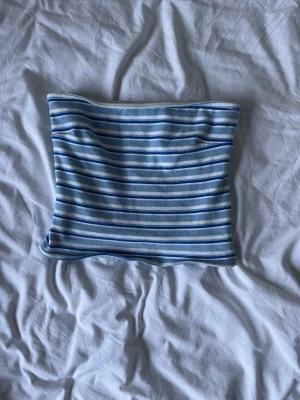 Blåvit randig bandeau topp - Säljer en bandeau topp med tunna axelband i blått och vitt randigt mönster. Toppen är croppad och har en slim passform, perfekt för sommardagar. Materialet känns mjukt och stretchigt, troligen bomull eller en bomullsblandning.