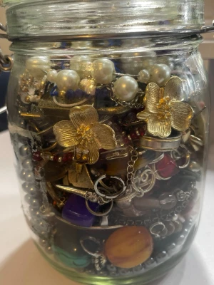 Mystery jewelry jar - En glasburk fylld med olika smycken och accessoarer som armband, halsband, ringar och örhängen m.m. i blandade färger och material. Det är blandat skick.