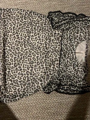 Leopardmönstrad volangklänning - Säljer en leopardmönstrad klänning med volangdetaljer och smockad överdel. Klänningen har korta ärmar med svarta kantband och är gjord i ett tunt, lätt material. Perfekt för dig som gillar djurmönster och vill sticka ut.