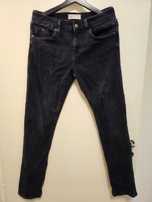 Colin's svarta jeans - Ett par jeans från Colin's Jeans i "Straight Fit"-modell. Jeansen har en klassisk design med fem fickor, bälteshällor och knappgylf. Det finns en läderlapp med "Colin's Jeans" präglat på linningen baktill och en mindre läderdetalj med nitar vid den högra framfickan.  Nytvättade med parfymfritt tvättmedel.