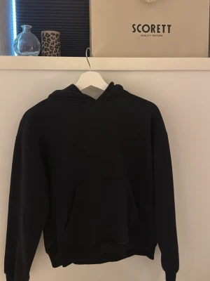 Svart hoodie från 157, storlek XS - En klassisk svart hoodie från 157 i storlek XS. Hoodien har en stor känguruficka framtill och en rymlig huva. Perfekt för en avslappnad och stilren look. Tillverkad i mjukt material som känns skönt mot huden.