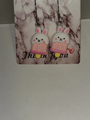 Söta kaninörhängen i pastell - Ett par gulliga örhängen med kaninformade hängen i vitt och rosa, dekorerade med små detaljer som rosa kinder och öron. Örhängens krokarna är i rostfritt stål. Finns flera örhängens par av dessa 