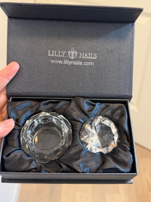 Kristallset från Lilly Nails Diamond Dappendish - Säljer ett exklusivt kristallset från Lilly Nails, perfekt för nagelarbete. Tex för att förvara monomer. Setet innehåller en rund kristallskål och en slipad kristallprisma, båda i transparent glas material. Levereras i en elegant svart presentask med sidenfoder. 