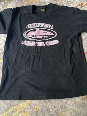 Svart t-shirt med tryck - Svart cortiez t-shirt i bomull med ett stort slitet tryck i rosa och vitt framtill. Klassisk rund halsringning och korta ärmar. Perfekt för dig som gillar en avslappnad och enkel stil.