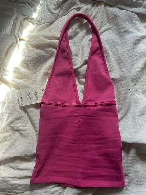 Rosa halterneck tröja  - Trendig rosa croppad topp med djup v-ringning och breda axelband. Tillverkad i ett stretchigt material som sitter snyggt och bekvämt. Perfekt för dig som vill ha en enkel men ändå statement topp till din outfit.