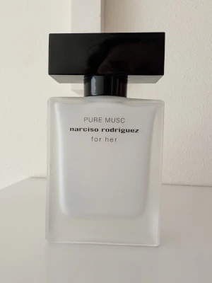 Narciso Rodriguez Pure Musc for Her - Minimalistisk parfymflaska i frostat glas med svart, rektangulärt lock. Doften är Pure Musc for Her från Narciso Rodriguez. Flaskan har en stilren och modern design med tydlig logotyp på framsidan. Använd ganska lite. 
