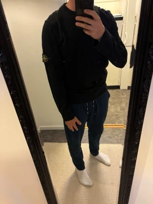 Svart sweatshirt från Stone Island - Svart sweatshirt från Stone Island med klassisk rund hals och ikonisk patch på vänster ärm. Tröjan har en clean look och är tillverkad i mjukt bomullsmaterial. Modell på bilden är 182 och väger 80kg. Den enda deffekten är lite lagning vid halsen(se sista bilden), men inget som man ser eller tänker på.