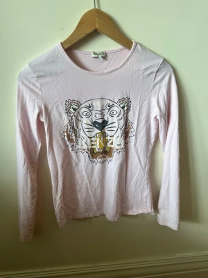 Ljusrosa långärmad topp från kenzo - Säljer en ljusrosa långärmad topp från kenzo. Toppen har rund halsringning och är gjord i mjukt bomullsmaterial. Perfekt för dig som vill ha en cool och unik detalj i garderoben.