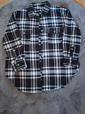 Svartvit rutig overshirt från Haily's - Säljer en svartvit rutig overshirt från Haily's i storlek L. Skjortan har två bröstfickor med knappar, klassisk krage och långa ärmar med manschett. Materialet är mjukt och känns som bomull, perfekt för lager på lager. Stängs med knappar framtill.