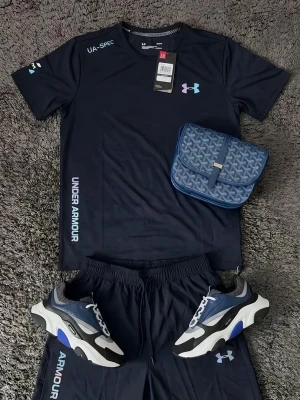 Mörkblått träningsset från Under Armour - Snyggt mörkblått träningsset från Under Armour med matchande t-shirt och shorts. Setet har vita och blå loggor samt tryck på både tröja och byxa. Materialet är lätt och andas, perfekt för träning eller sport. Ingår även ett par sportiga sneakers i svart, blått och vitt.