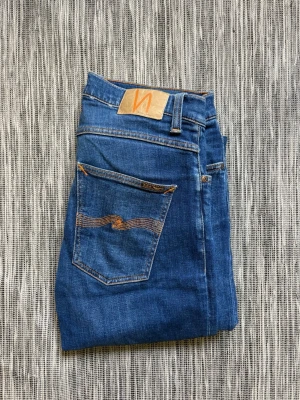 Nudie Jeans grim Tim - Snygga blå jeans från Nudie Jeans med klassisk femficksmodell och smal passform. Jeansen har orange sömmar och en ikonisk vågdetalj på bakfickan. Tillverkade i denim med en lätt tvättad look och normal midja. Modell grim Tim. Ett par som blir snyggare ju mer man använder dom, dessa är väldigt sparsamt använda!
