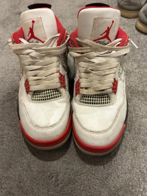 Vita och röda Air Jordan 4 sneakers - Säljer ett par Air Jordan 4 sneakers i vitt, rött och svart. Skorna har klassisk mesh på sidorna, röda detaljer och svart hälpanel. Tjock sula och ikonisk Jumpman-logga på plösen. Perfekta för dig som gillar streetwear och basketstil. Titta på pris…