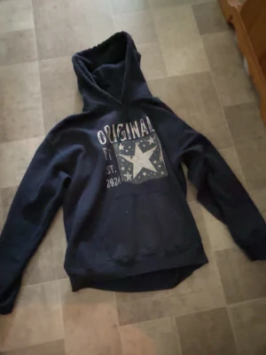 Scndi hoodie mörkblå - Säljer en scndi hoodie med texten 'ORIGINAL' på bröstet. Hoodien har huva och magficka, samt tryck med mindre stjärnor runt den stora. Perfekt för dig som gillar en avslappnad stil