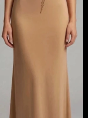 Beige långklänning med paljettdetaljer - Elegant beige långklänning med glittriga paljettdetaljer upptill och asymmetriskt mönster. Klänningen har en figurnära passform och är ärmlös, vilket ger en stilren och modern look. Perfekt för speciella tillfällen när du vill sticka ut. Brun.