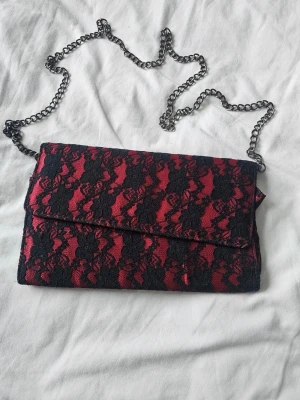 RARE FIND! Vintage 90-tal Aftonväska i Röd Satin & Svart Spets – Nyskick! - Mått: 26 × 15 cm (rymlig, rymmer utan problem en modern smartphone, plånbok och smink)Ett unikt tillfälle för dig som älskar vintage! Denna fantastiska aftonväska/kuvertväska från 90-talet är ett riktigt "rare find".