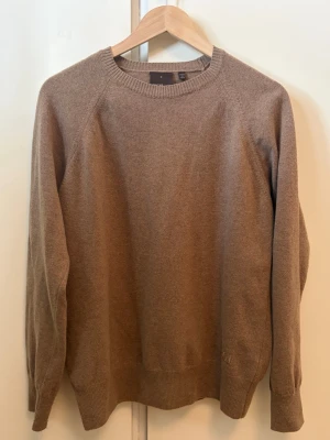 Stickad tröja från Oscar Jacobsson - En enkel och stilren beige stickad tröja med rund halsringning och långa ärmar. Tröjan har ribbade muddar vid ärmslut och nederkant. Tillverkad i mjuk ullmix som känns skön mot huden. Perfekt för lager på lager under kyliga dagar.