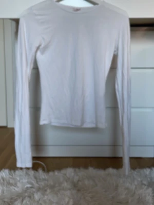 Vit långärmad topp i bomull - En enkel och stilren vit långärmad topp med rund hals. Tillverkad i mjuk bomull och har en normal passform som funkar till det mesta. Perfekt basplagg att ha i garderoben.