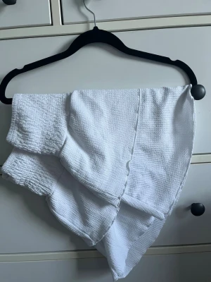 Vit asymmetrisk kjol med volanger - Säljer en vit kjol med flera lager volanger. Perfekt för dig som vill ha en unik och trendig look till sommaren eller våren.