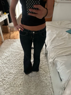 Mörkblå lågmidjade jeans - Snygga svarta bootcut jeans med markerade vita sömmar och klassiska fem fickor. Jeansen har utsvängda ben och låg midja, vilket ger en retro och trendig vibe. Perfekta för dig som gillar en cool och avslappnad stil.