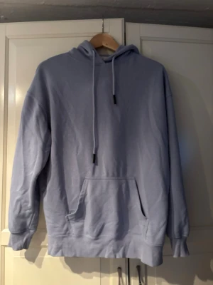 Ljusblå oversized hoodie - En ljusblå hoodie med huva och dragsnören. Hoodien har en stor magficka och ribbade muddar vid ärmslut och nederkant. Är ganska nopprig.