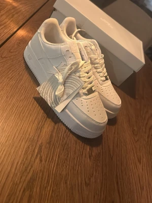 Nike Air Force 1 vita sneakers - Klassiska Nike Air Force 1 sneakers i helvitt läder med perforerad tå, vita skosnören och diskret Nike-logga på sidan. Tidlös och clean design som passar till det mesta. Kommer med originalkartong och tags kvar. köptes som present till min bror han fick flera par skor han behlvde ej dessa. Använda en gång på skolavslutningen!!