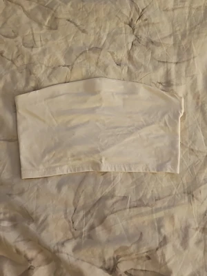 Vit bandeau tubtopp från 157 - Säljer en enkel och stilren vit bandeau tubtopp från 157 i storlek XS/S. Toppen är ärmlös och axelbandslös, perfekt för varma dagar eller som layering-plagg. Materialet känns mjukt och stretchigt, vilket gör den bekväm att bära.