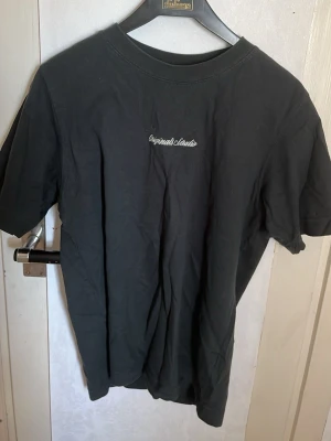 Svart t-shirt från Jack & Jones - Svart t-shirt från Jack & Jones med liten vit text på bröstet. Klassisk rund halsringning och korta ärmar. Skön och enkel modell i bomull, perfekt till jeans eller shorts.