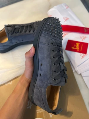 Christian Louboutin gråa - Säljer ett par gråa sneakers i mocka från Christian Louboutin. Skorna har nitar på, matchande grå skosnören. Insidan är beige och designen är riktigt edgy och unik. Perfekta för dig som vill sticka ut med din stil.