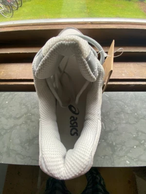 Gråa Asics sneakers i mesh och syntet - Snygga sneakers från Asics i ljusgrå färg med ovandel i mesh och syntetmaterial. Skorna har klassisk snörning och vadderad plös för extra komfort. Perfekta för dig som gillar stilrena och sportiga sneakers.