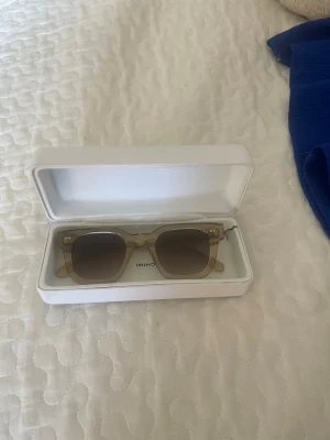 Beige fyrkantiga solglasögon Chimi - Snygga solglasögon från Chimi med transparent beige båge och fyrkantig form. Glasen är tonade i brunt och bågarna är tillverkade i syntetmaterial. Perfekta för att lyfta din stil under soliga dagar.