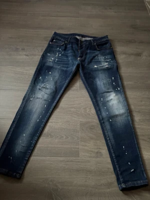Mörkblå Dsquared2 jeans  - Säljer ett par mörkblå jeans från Dsquared2 med coola slitningar och färgstänk. 