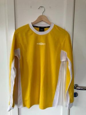 Vintage tröja från Umbro - Snygg gul långärmad sporttröja från Umbro med vita detaljer längs ärmar och sidor. Tröjan har rund halsringning och är tillverkad i ett lätt och funktionellt material