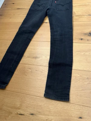 Svarta raka jeans från Levi's - Säljer ett par svarta jeans från Levi's med klassiska bakfickor och rakt ben. Jeansen har en diskret tvätt och är tillverkade i slitstark denim. Perfekta för dig som gillar en clean och tidlös look.