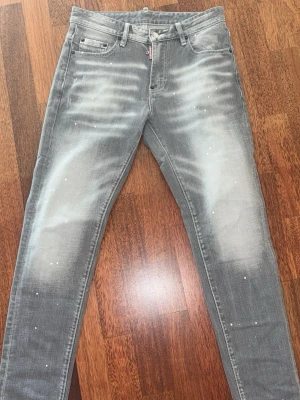 Gråa DSQUARED2 Jeans  - Säljer ett par grå skinny jeans från Dsquared2 med slitna detaljer och vita färgstänk. Jeansen har fem fickor, bälteshällor och dragkedjegylf. Snygg tvättad look som passar perfekt till streetwear-stilen.