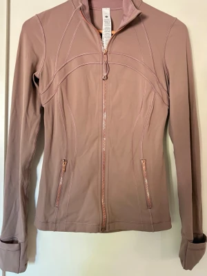 Lululemon zip jacka - Säljer min älskade Lululemon träningsjacka då jag har köpt en annan och inte använder denhär så mycket. Den är beige/rosa/brun och har en superfin rosé färgad dragkedja💓skriv för fler frågor!