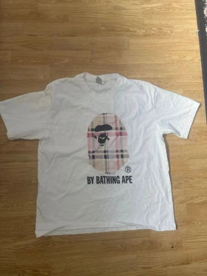 Vit t-shirt By Bathing Ape  - Säljer en Rep BAPE t-shirt med stort som är even tryckt på bröstet och texten 'BY BATHING APE' under. 
