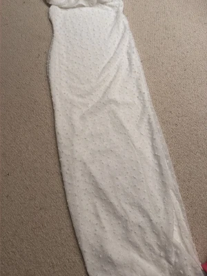 Vit långklänning med prickigt mönster - Elegant vit långklänning med diskret prickigt mönster. Klänningen har en smal passform och är ärmlös, vilket ger en stilren och modern look. Perfekt för speciella tillfällen under sommaren.