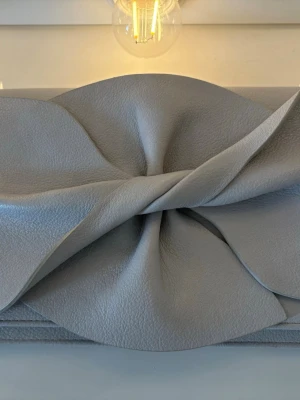  Tiamo axelväska i ljusgrå/beige  - Säljer en superfin Tiamo-väska i en tidlös ljusgrå/beige nyans med silverkedja. Elegant knutdetalj framtill som passar både till vardag och fest. Väskan är rymlig trots sin smidiga storlek och matchar i princip allt. I perfekt skick! 