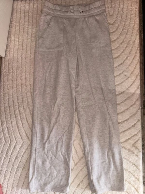 Ljusgrå mjukisbyxor med raka ben - Säljer ett par ljusgrå mjukisbyxor med raka ben och resår i midjan. Byxorna har två sidofickor och är gjorda i ett mjukt, stretchigt material som känns skönt mot huden. Perfekta för chill dagar hemma eller när du vill vara bekväm.