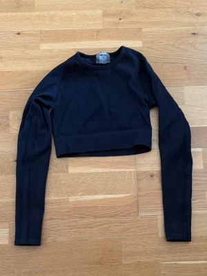 Svart croppad topp aim’n - Snygg svart croppad topp med lång ärm och ribbad struktur. Perfekt till höga jeans eller kjol. Enkel och stilren design med rund halsringning.