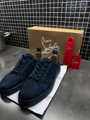 Mörkblå sneakers från Christian Louboutin - Snygga mörkblå sneakers i mocka från Christian Louboutin med klassisk låg siluett och matchande mörkblå snörning. Skorna har en stilren design med diskreta sömmar och en bekväm innersula i ljust läder. Perfekta för dig som vill ha något exklusivt och trendigt.