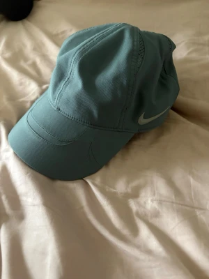  Nike NOCTA keps - Snygg blågrön keps från Nike NOCTA med klassisk böjd skärm och justerbar rem bak. Kepsen har en diskret Nike Swoosh på sidan och NOCTA-logga broderad bak. Tillverkad i slitstarkt tyg, perfekt för en sportig och trendig look.