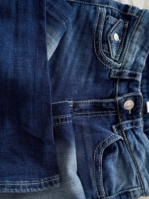 Blå jeans med broderade detaljer - Säljer ett par snygga blå jeans med coola broderade detaljer på bakfickan och dekorativa sömmar. Jeansen har klassisk femficksmodell, silverfärgade knappar och en tvättad look. Perfekta för dig som vill ha något extra till din outfit.