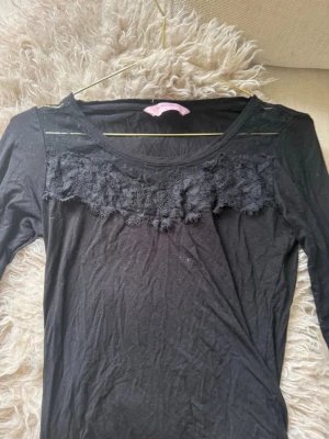 Svart topp med spetsdetaljer - Snygg svart långärmad topp med transparent mesh och spetsdetaljer över bröstet. Toppen har rund halsringning och prickigt mönster i meshen. Perfekt för dig som gillar en feminin och trendig stil.🖤