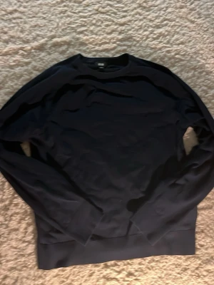 Mörkblå tröja från Uniqlo - En stilren mörkblå tröja från Uniqlo med rund halsringning och långa ärmar. Tröjan har ribbade muddar vid ärmslut och nederkant, vilket ger en klassisk och enkel look. Perfekt att matcha med jeans eller kjol.